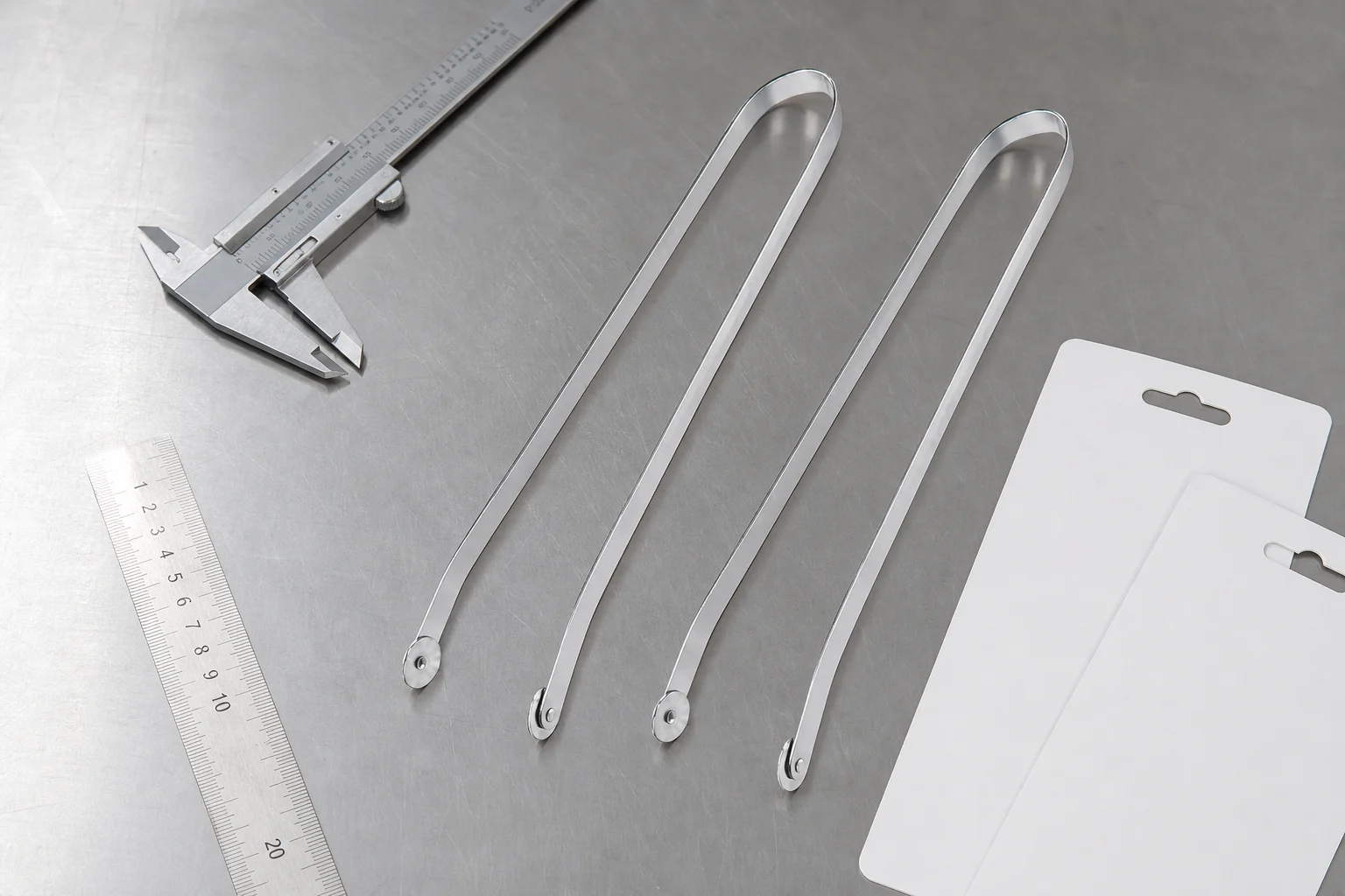 Clean stainless steel BBQ tongs inspected on a stainless QC bench with a caliper, ruler, and blank hang-card sleeves